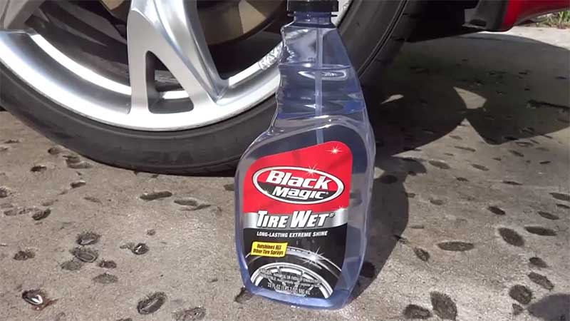 Bottle of tire shine spray on asphalt next to a red car